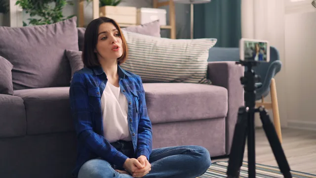 Adult woman recording video indoors on a smartphone, sitting cross-legged on the floor. Kontrollér aktuelle krav til reklamemarkering