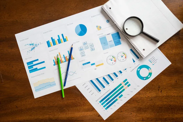 Overhead view of financial charts, magnifying glass, and stationery on wooden table. Tillad ærlige sammenligninger uden krav om positiv omtale